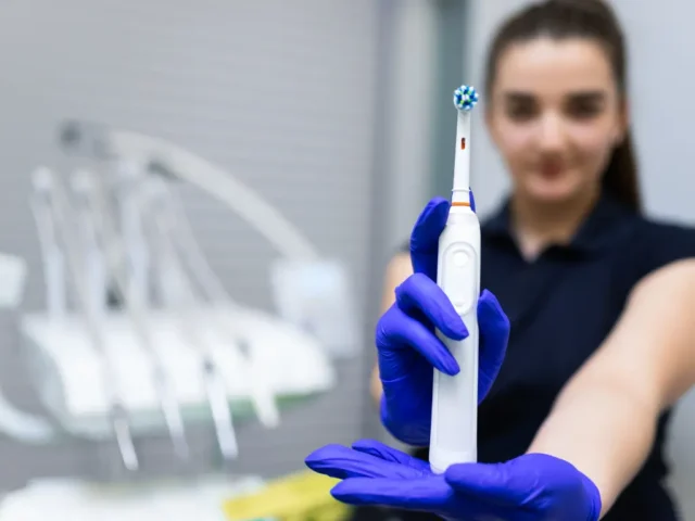 Dental professional wearing gloves holding an electric toothbrush in a clinic